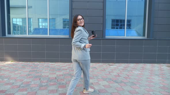 Young Woman in a Formal Suit and with a Plastic Glass Dancing on the Street