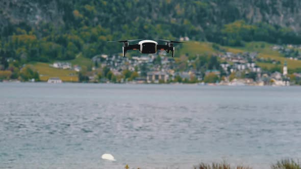 Drone with Rotating Propellers Hanging in the Air on a Background of Lake and Mountains