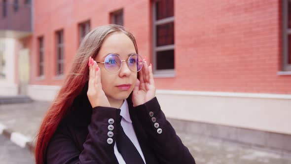 Young Woman in Business Suit Adjusting Glasses on Face Standing on City Street