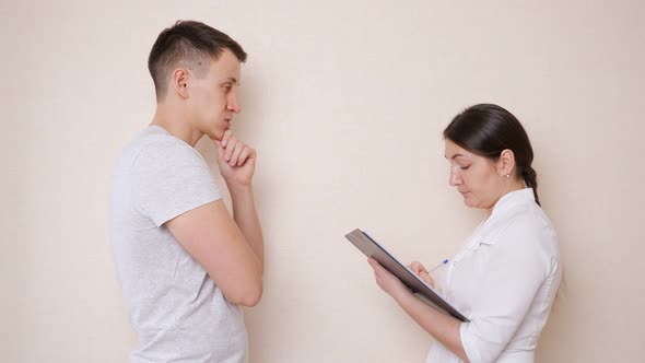 Female Doctor Talking to a Male Patient and Fills Out a Document Taking Anamnesis