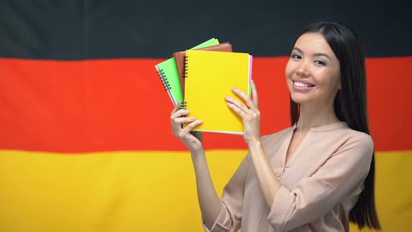 Cheerful Female Showing Copybooks Against German Flag, Foreign Language Courses