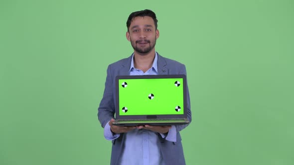 Happy Young Bearded Persian Businessman Talking While Showing Laptop