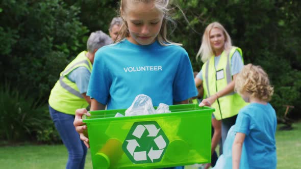 Smiling caucasian girl holding recycling box picking up litter with volunteers in field