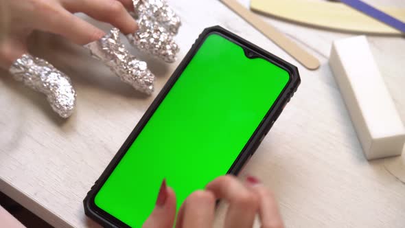 A Girl During a Manicure Uses a Smartphone with a Green Screen