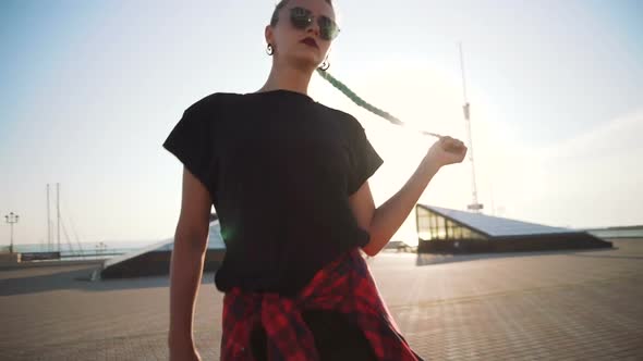 Young Stylish Funky Girl with Green Hair Riding Roller Skates and Dancing Near Sea Port During