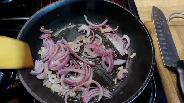 Human Hand Stirring Fried Onion in Frying Pan in Domestic Kitchen for Cooking Food on Kitchen Stove
