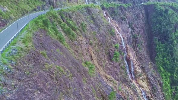 Camera Flies Along Highway on Steep Cliff and Waterfall