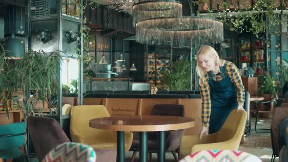 Cheerful Waitress is Rearranging Furniture in the Restaurant