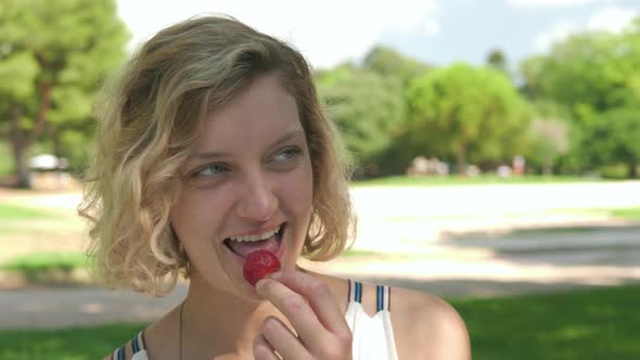 Close Up of a Woman Eating a Strawberry While on a Picnic Date in a Park, Slow Motion