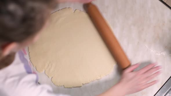 girl rolls dough on the table with a rolling pin