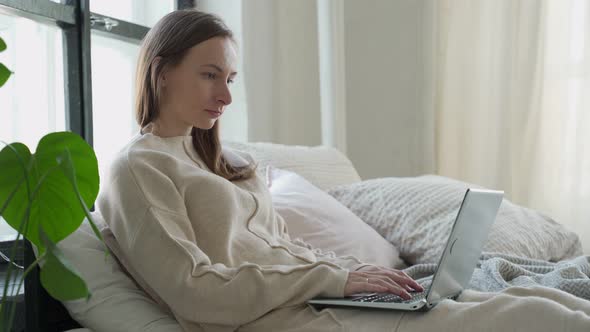 Relaxed Brunette Young Woman Using Laptop in Bed at Home