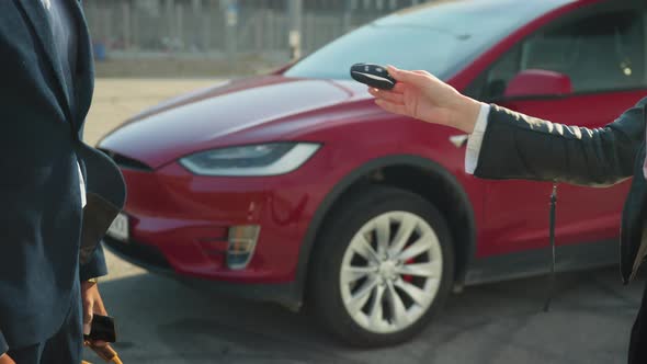 Close Up of Female Seller Presenting Keys From Red Electric Car to Male Customer