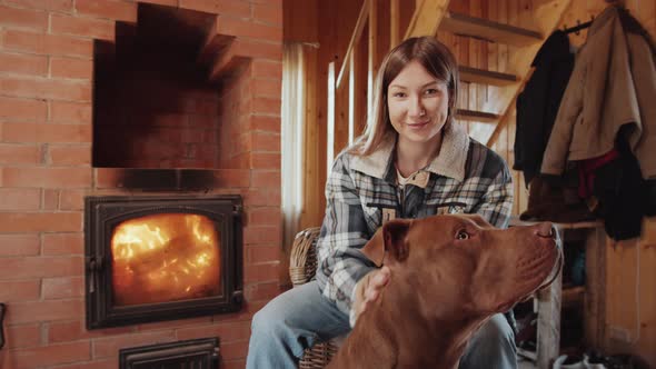 Portrait of Cheerful Woman Petting Dog by Fireplace in Farmhouse