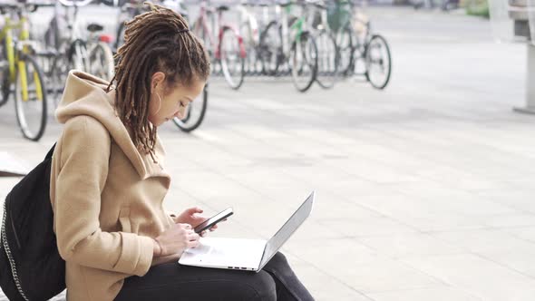 young woman outdoors using smart phone and laptop computer