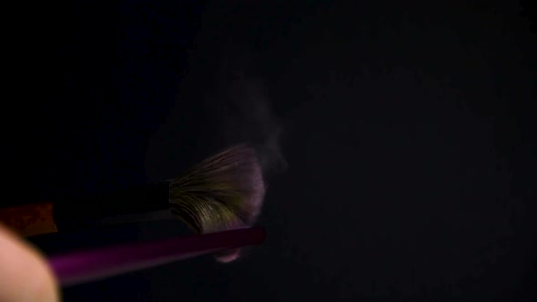 slow motion of a make up brush with pink powder explosion and burst on black background