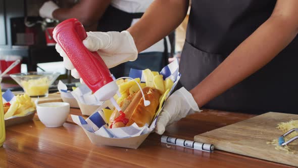 Mid section of african american woman wearing apron putting ketchup over hot dog in food truck