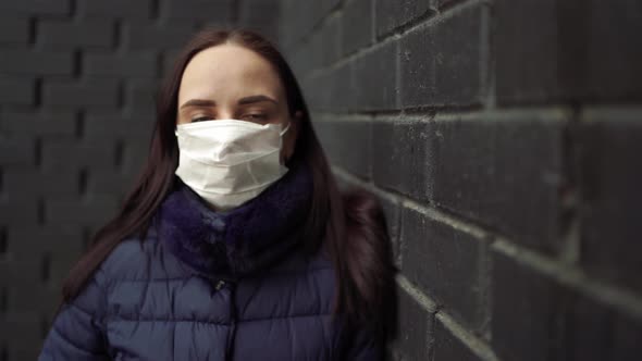 Portrait of Young Woman in Medical Mask on Her Face Against Black Brick Wall