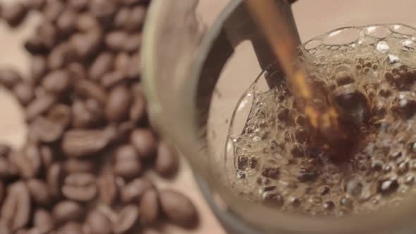 Pouring fresh coffee into a pot with coffee beans background