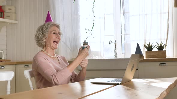 Retired Woman Blows Cracker with Confetti Against Laptop