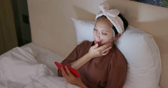 Woman apply paper mask and watch on cellphone at home