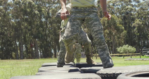Diverse group of soldiers running through car tyres on army obstacle course alt