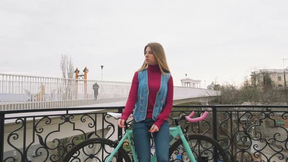 A Young Hipster Girl Standing with Fixed Gear Bike at City Centre Near Bridge Slow Motion
