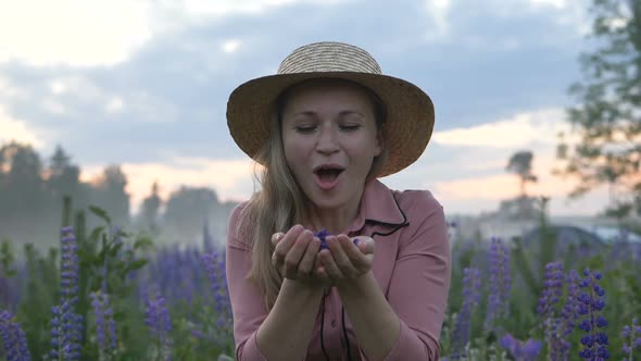 Happy Girl in a Hat Blows Off Flower Petals From Her Hands and Looks at the Camera in Slow Motion