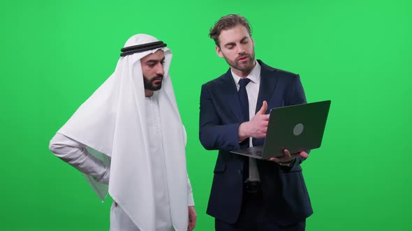 Businessman in a Suit Uses a Laptop and Communicate with a Arab Business Partner in a White Kandura