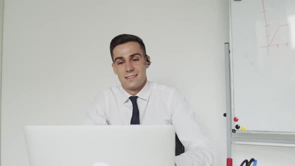 Happy Office Manager with a Earset Provides Online Advice on a Laptop in Office