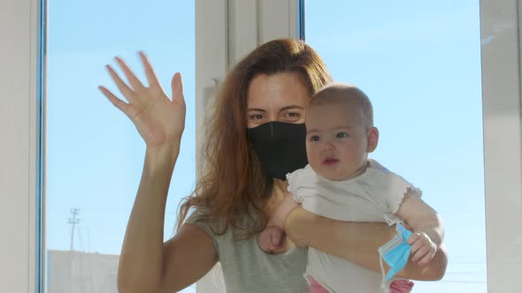 Mother in Medical Mask Communicated with Baby on Hands Through Glass Window