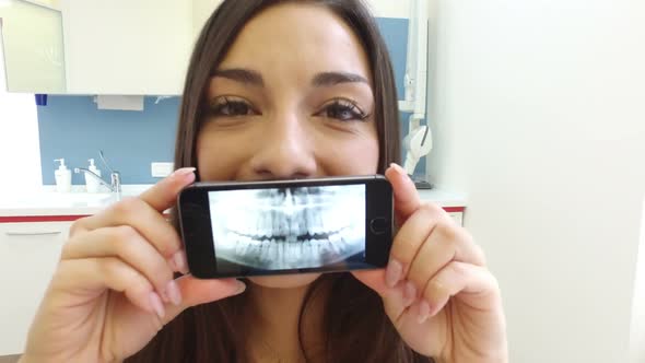 Close up of happy brunette woman holding smartphone with photo of dental X- ray