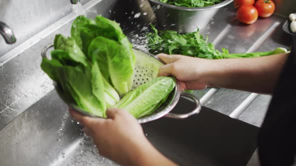 Caucasian female chef washing vegetables in colander in restaurant kitchen