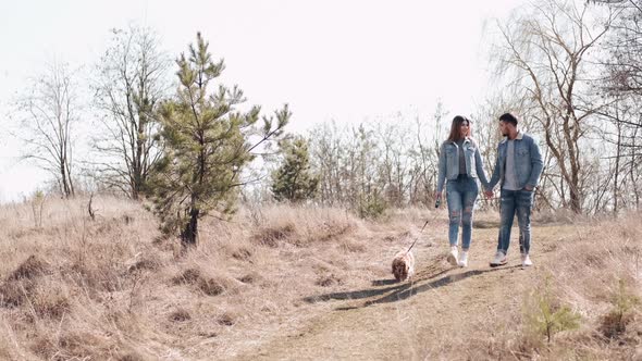 Young Man and Woman in Denim Are Walking in the Wheat Field with a Dog