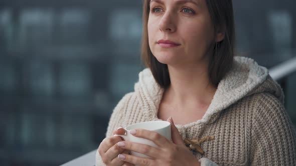 Woman Stays on Balcony During Snowfall with Cup of Hot Coffee or Tea