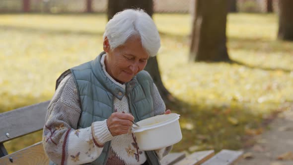 An Elderly Woman Eating Charity Meal While Sitting on the Bench in the Park