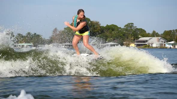 A young woman wake surfing behind a boat on a lake.