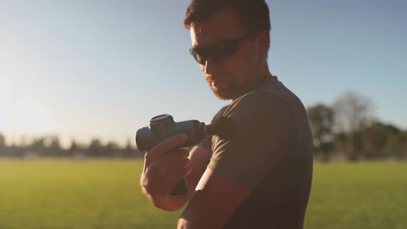 An Athlete Massages with a Percussion Therapy Gun to Relieve the Pain of Muscle Aches After a