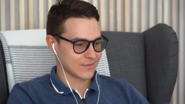 Young handsome brunette man sits in gray chair, listens to music, keep calm and relax.