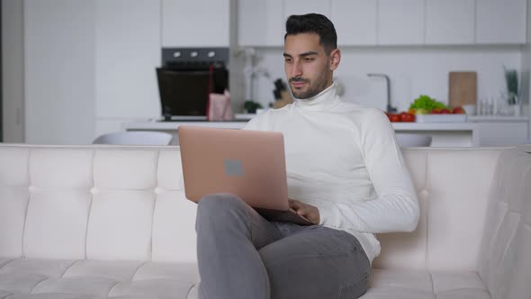 Confident Middle Eastern Businessman Sitting on Couch Surfing Internet on Laptop