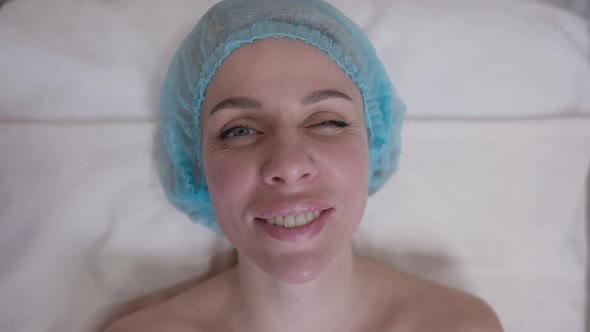 Top View Face of Naked Woman in Shower Hat Winking Looking at Camera Smiling