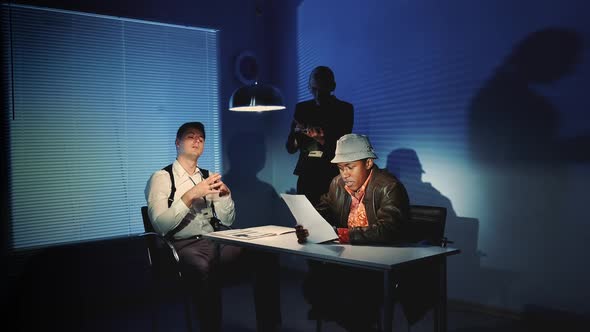 In the Interrogation Room Police Detective Showing Facts of Suspected Criminals