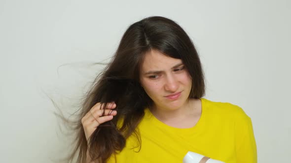 A Brunette Woman Dries Her Hair with a Hair Dryer Looks at Her Hair with a Dissatisfied Look