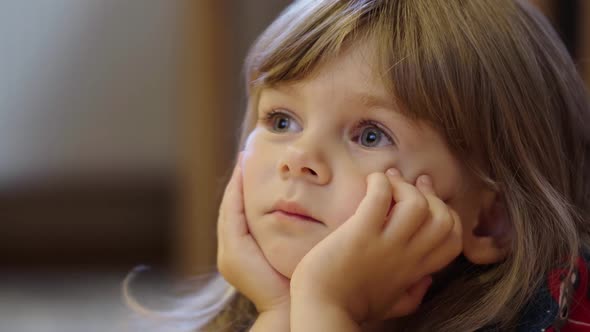 Portrait of a Cute Little Girl Watching TV Intently with Her Hands Supporting Her Face