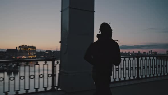 Silhouette of Active African American Guy Running on City Bridge in Evening Practicing Sport