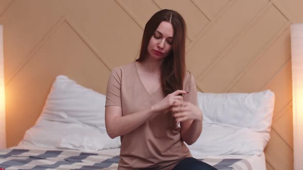 Woman is Sitting on Bed and Combing Long Hair with Hands Front View