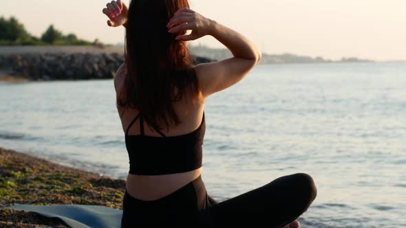 A yogi woman sits in a lotus position on the seashore and looks at the sea dawn of the sun.