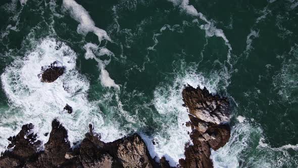Aerial - Rough water leaving beautiful patterns along rocky coastline, top-down shot, flying horizon