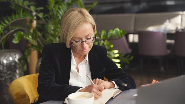 Portrait of Middle Aged Business Woman Writing in Notebook