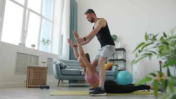 Helpful Boyfriend Supporting Young Lady During Stretching Exercise Doing Sports Indoors at Home