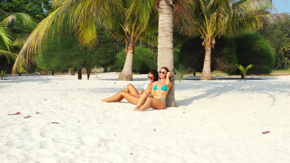 Beautiful smiling ladies on photoshoot having fun at the beach on summer white sand and blue 4K back